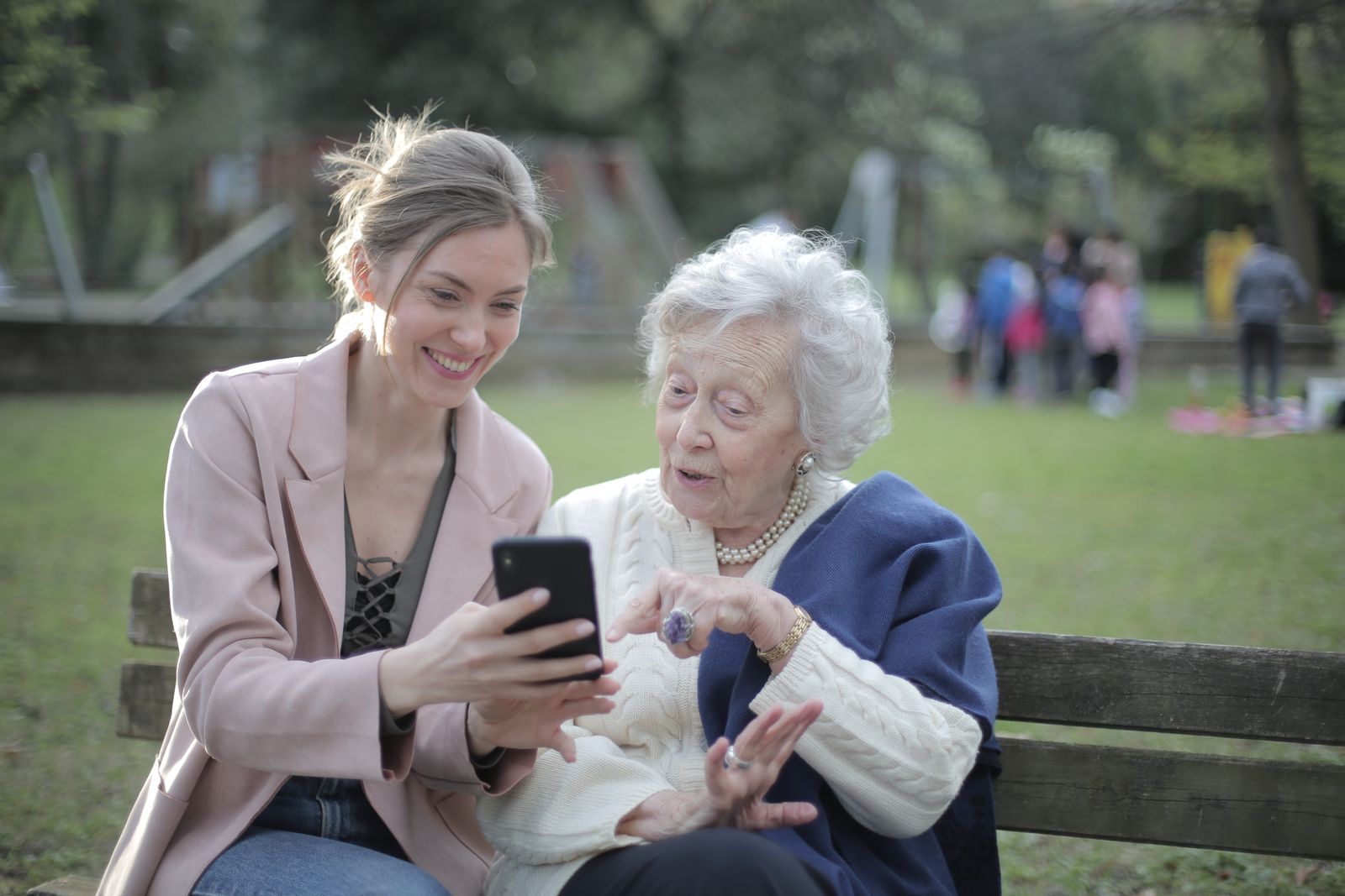 Two women sitting on a park bench, looking at a phone together